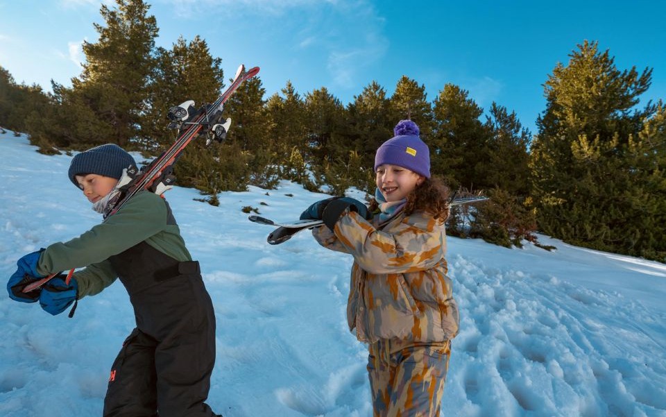 Kids wearing their skis on their shoulders